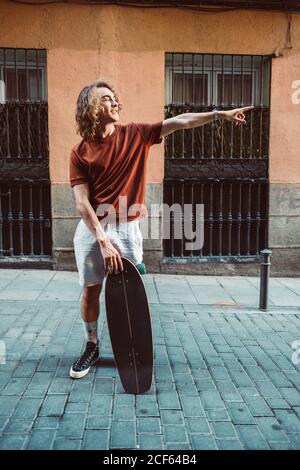Schöner sportlicher Mann hält Longboard, während er im Sommer in der Stadt steht City Street Stockfoto