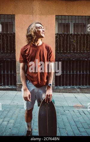 Schöner sportlicher Mann hält Longboard, während er im Sommer in der Stadt steht City Street Stockfoto