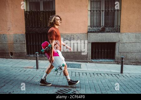 Seitenansicht eines gut aussehenden sportlichen Mannes, der beim Gehen Longboard hält Auf der Stadt Sommer Stadt Straße Stockfoto