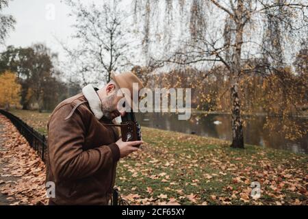 Nicht erkennbare Seitenansicht des erwachsenen Mannes mit Retro-Fotokamera Stehen auf trockenen Blättern im ruhigen Herbstpark im Herbst Stockfoto