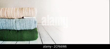 Kuscheliger Herbst-Bannerstapel aus warmen Strickpullover in Pastell Farben und die Inschrift Oktober auf einem hellen Holztisch Im Zimmer Stockfoto