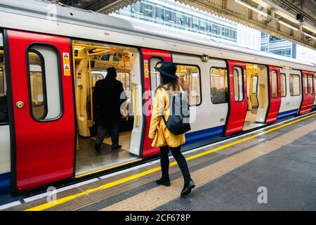 Seitenansicht einer glücklichen, stilvollen Frau, die in einen U-Bahn-Zug auf dem Bahnsteig am Bahnhof in London, Großbritannien, einfährt Stockfoto