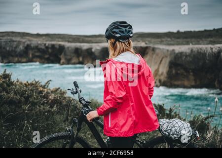 Rückansicht einer anonymen jungen Frau mit dem Mountainbike, die auf einer Klippe auf Meeresgrund läuft Stockfoto