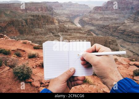 Crop Mann macht Notizen in Tagebuch, während mit Ruhe an Klippenrand im Canyon in den USA Stockfoto