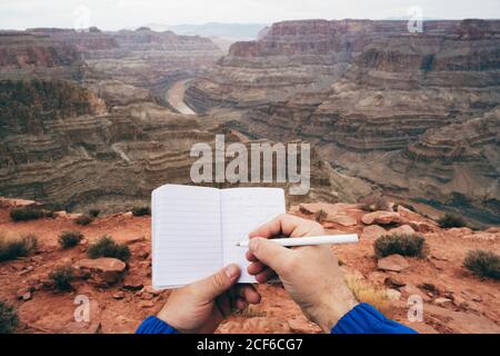 Crop Mann macht Notizen in Tagebuch, während mit Ruhe an Klippenrand im Canyon in den USA Stockfoto