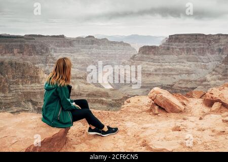 Seitenansicht einer ruhigen Frau in einer Jacke mit Rucksack, die sich auf dem Felsen ausruhte und den Canyon in den USA betrat Stockfoto