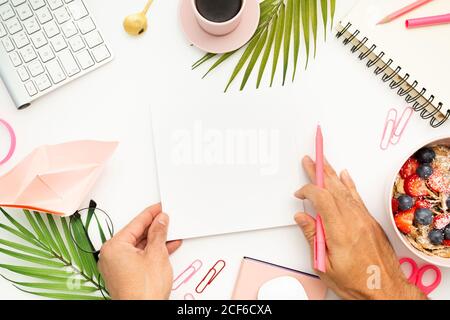 Draufsicht auf anonymen Mann mit leerem Blatt Papier Und Stift sitzen am weißen Tisch mit Frühstückschale und tasse Espresso Stockfoto