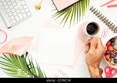 Draufsicht auf anonymen Mann, der am Tisch mit Tasse sitzt Von heißem Espresso und arbeiten in kreativen Arbeitsplatz mit Papier Und Schreibwaren Stockfoto