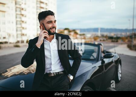 Seitenansicht des Geschäftsmannes, der vor einem Cabriolet telefoniert. Stockfoto
