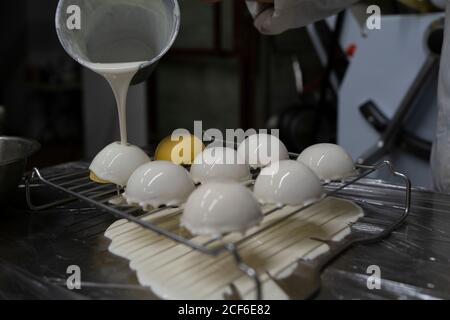 Crop Person Gießen weißen Spiegel Glasur auf leckere gelbe Mousse Kuchen auf Metallgitter in der Küche angeordnet Stockfoto