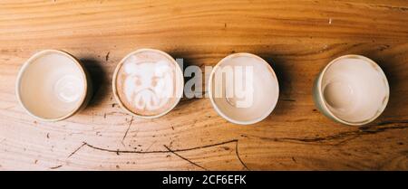 Draufsicht der Zeichnung des Schweins auf der Oberfläche von Cappuccino und Leere Tassen auf altem Holzhintergrund angeordnet Stockfoto