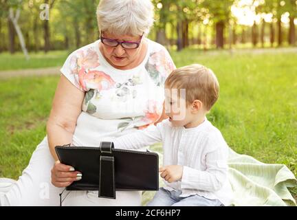 Glückliche Großmutter und Enkel sind mit digitalen Tablet in der parken Stockfoto