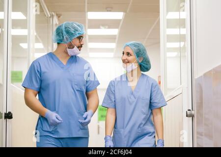 Chirurgen-Mitchirurgen, Mann und Frau unterhalten sich, während sie zum Operationssaal gehen Stockfoto