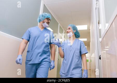 Chirurgen-Mitchirurgen, Mann und Frau unterhalten sich, während sie zum Operationssaal gehen Stockfoto