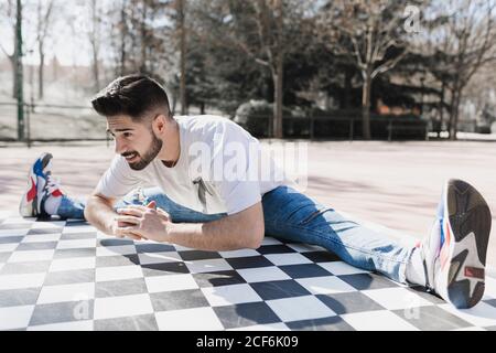 Junge bärtige Kerl in Freizeitkleidung tun Bein Split in parken bei sonnigem Wetter Stockfoto