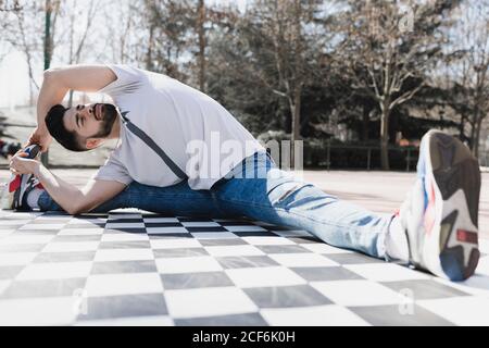 Junge bärtige Kerl in Freizeitkleidung tun Bein Split in parken bei sonnigem Wetter Stockfoto