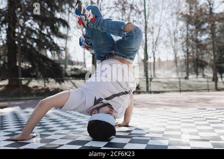 Junge bärtige Kerl in Freizeitkleidung tun Kopfstand im Park Bei sonnigem Wetter Stockfoto