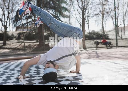 Junge bärtige Kerl in Freizeitkleidung tun Kopfstand im Park Bei sonnigem Wetter Stockfoto