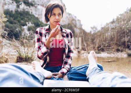 Crop Mann liegt auf kariert mit Frau sitzt in der Nähe und beißen Erdbeere genießen Zeit zusammen auf Picknick in der Natur Stockfoto
