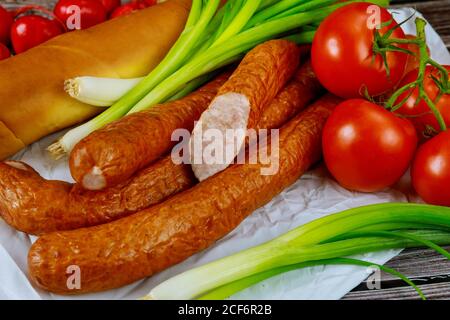 Europäische Räucherwurst mit grünen Zwiebeln und Brot auf Holzhintergrund. Stockfoto
