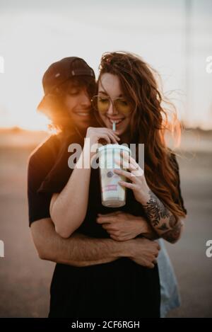 Junge stilvolle Jugendliche umarmen glücklich wille stehend in abgelegenen ländlichen Feld mit warmen Sonnenuntergang Licht trinken Milchshake Stockfoto