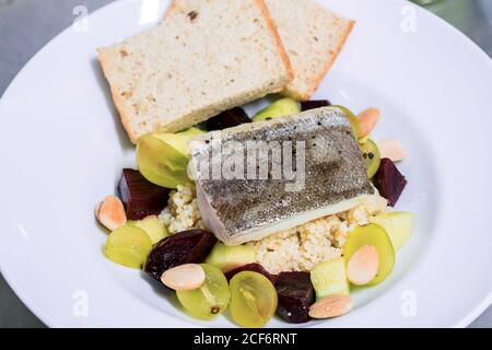 Von oben von köstlichen Gericht mit gekochtem Fisch serviert mit Quinoa-Salat mit Trauben und Rote Bete auf weißem Teller Mit Brotscheiben Stockfoto