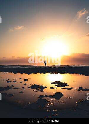 Silhouette einer anonymen Person, die am Ufer in der Nähe von ruhigem Wasser gegen Sonnenuntergang Himmel am Abend auf Fuerteventura Insel, Spanien Stockfoto