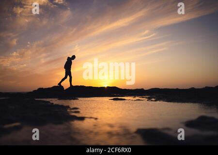 Silhouette einer anonymen Person, die am Ufer in der Nähe von ruhigem Wasser gegen Sonnenuntergang Himmel am Abend auf Fuerteventura Insel, Spanien Stockfoto