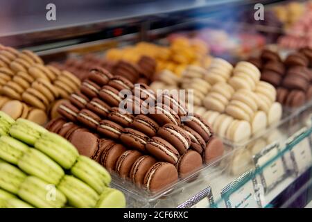 Viele bunte leckere Makronen in verschiedenen Farben mit verschiedenen Füllungen Und schmeckt durch Farben in Behälter, die auf der Schau stehen Fenster in der Konditorei Stockfoto