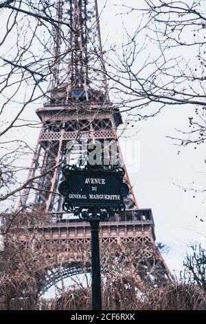 Landschaftlich schöne Aussicht auf schwarze Stahl Straße Zeichen gegen verschwommen Eiffelturm und blattlose Äste am warmen Frühlingstag In Paris Stockfoto