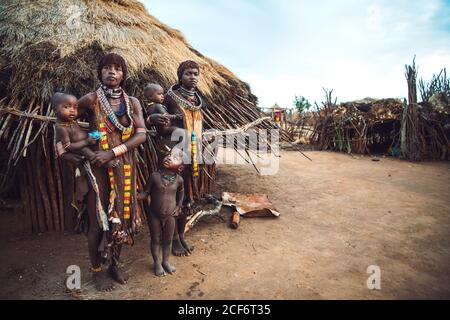 Omo Valley, Äthiopien - 08. November 2018: Zwei Frauen des Stammes Hamer stehen mit Babys gegen Dorfhütte. Omo Valley, Äthiopien Stockfoto