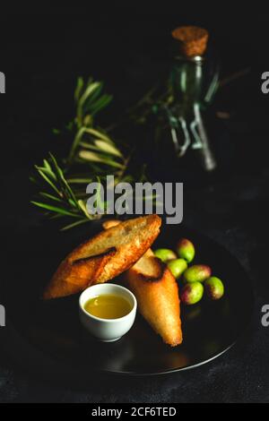 Frisches spanisches Olivenöl extra vergine mit Oliven und alten Olivenzweig auf dunklem Hintergrund gesunde Ernährung mediterrane Ernährung. Vegan. Vegetarisch. Geröstetes Brot Stockfoto