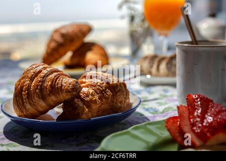 Hausgemachtes komplettes Brunch-Frühstück im Sonnenlicht mit Croissants, Erdbeeren, Tee oder Kaffee und Orangensaft Stockfoto