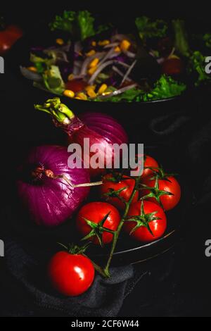 Gesundes veganes Essen mit frischem Salat, Kirschtomaten, roten Zwiebeln und Mais auf dunklem Hintergrund Stockfoto