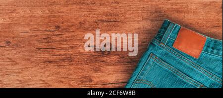 Jeans Hose auf Holz Banner Panorama Hintergrund. Draufsicht auf braune Holzstruktur und blaue Denim-Kleidung für Männer und Frauen mit Lederrückenetikett Stockfoto