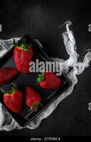 Rote und frische Erdbeeren lagen flach in schwarzer Schale Stockfoto