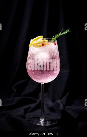 Gin Tonic Cocktail mit rosa Tonic Water, rosa Pfeffer, Rosmarin, Minze, Zimt, Zitrone und Orange auf dunklem Hintergrund Stockfoto