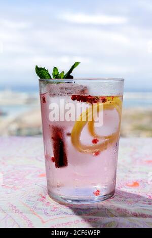 Gin Tonic Cocktail mit rosa Tonic Water, rosa Pfeffer, Rosmarin, Minze, Zimt, Zitrone und Orange im Sonnenlicht auf einem Restauranttisch Stockfoto