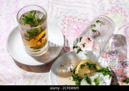 Eistee mit gefrorenen Wasserwürfeln verschüttet auf Untertasse mit Zitrone und Minze Stockfoto