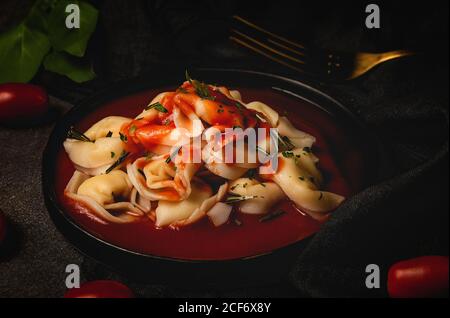 Gekochte Ravioli mit Tomatensauce und Kräutern in Schüssel weiter Auf den Tisch zu Gabel und Serviette Stockfoto