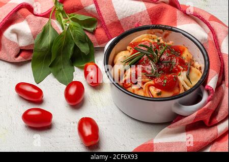 Gekochte Ravioli mit Tomatensauce und Kräutern auf Sauce Pfanne Kasserolle neben Tomaten auf Tuch in einem Tisch Stockfoto