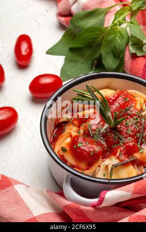Gekochte Ravioli mit Tomatensauce und Kräutern auf Sauce Pfanne Kasserolle neben Tomaten auf Tuch in einem Tisch Stockfoto