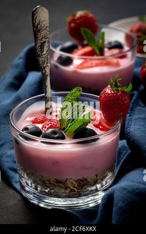 Hausgemachter Joghurt mit Erdbeeren, Heidelbeeren und Getreide mit dunklem Hintergrund und Sonnenlicht.gesundes Lebensmittelkonzept.Veganes Essen Stockfoto
