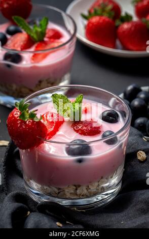 Hausgemachter Joghurt mit Erdbeeren, Heidelbeeren und Getreide mit dunklem Hintergrund und Sonnenlicht.gesundes Lebensmittelkonzept.Veganes Essen Stockfoto