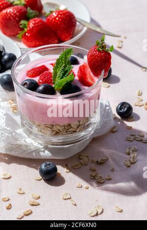 Hausgemachter Joghurt mit Erdbeeren, Heidelbeeren und Getreide mit rosa Tischdecke und Sonnenlicht.gesundes Lebensmittelkonzept.Veganes Essen Stockfoto