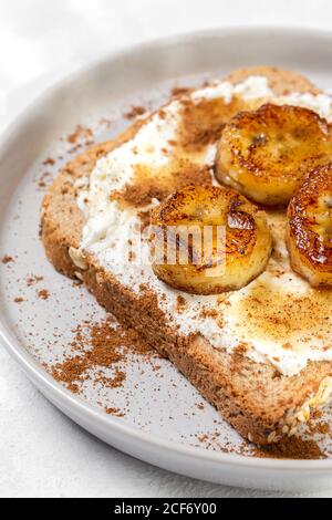 Hausgemachtes geröstetes Brot mit Frischkäse, gebratener Banane, Honig und Zimt.Vegetarisches Essen.gesundes Lebensmittelkonzept. Stockfoto