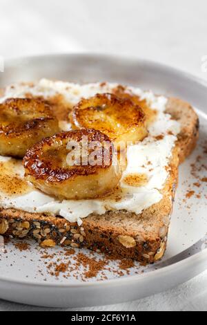 Hausgemachtes geröstetes Brot mit Frischkäse, gebratener Banane, Honig und Zimt.Vegetarisches Essen.gesundes Lebensmittelkonzept. Stockfoto