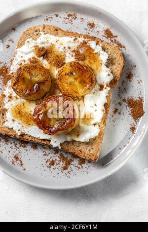 Hausgemachtes geröstetes Brot von oben mit Frischkäse, gebratener Banane, Honig und Zimt.Vegetarisches Essen.gesundes Lebensmittelkonzept. Stockfoto