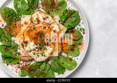 Hausgemachtes geröstetes Brot mit Spiegelei, Spinat und aromatischen Kräutern auf weißem Hintergrund.Vegetarisches Essen.gesundes Lebensmittelkonzept. Stockfoto