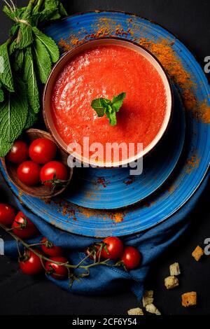 Gesunde hausgemachte Tomatensuppe mit Brot, Minze und Olivenöl auf dunklem Hintergrund von oben.Veganes Lebensmittelkonzept Stockfoto